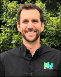 Portrait of Dave Golden, Assistant Commissioner of New Jersey DEP Fish & Wildlife, smiling outdoors in front of green foliage while wearing a black New Jersey Fish & Wildlife button-down shirt.
