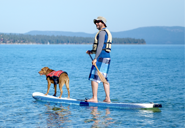 Man wearing a life jacket while paddleboarding with his dog.