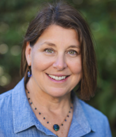 Portrait of Debbie Colbert, Director of the Oregon Department of Fish and Wildlife, smiling outdoors in a blue shirt and necklace.