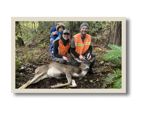 Two hunters in blaze orange kneel beside a harvested deer in a forest, with a child in a backpack carrier smiling in the background.